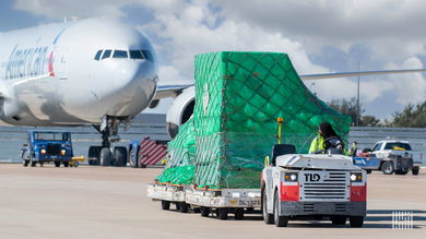 An airport tug pulls a cargo wagon in front of a white jet.