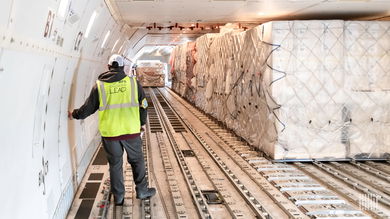 A man with a yellow vest inside the cargo bay of a large jet with large containers on the floor.