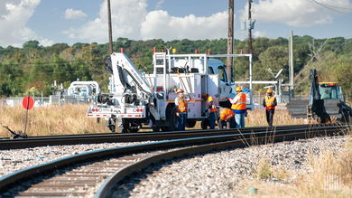 Workers stand next to a machine that is sitting on railroad track.