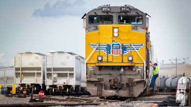 A Union Pacific train is parked in a rail yard next to some hopper rail cars.