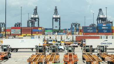 A view of cranes, trailers, containers and trucks at a port on a sunny day.