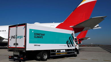 A box van with IAG Cargo lettering and green banner "Constant Climate" on the side in front of a large jet with a red tail.