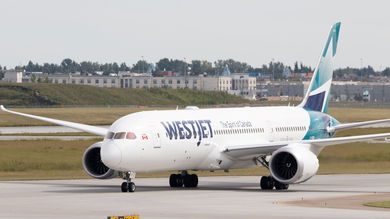 A jet with teal accents and WestJet logo rolls on a runway.