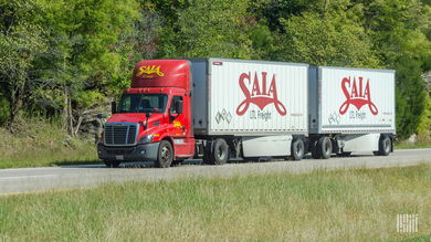 A red Saia tractor pulling two white Saia LTL trailers on highway
