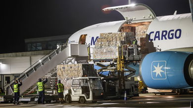 A cargo jet with light-blue engine trim being unloaded at night, with cargo door open.