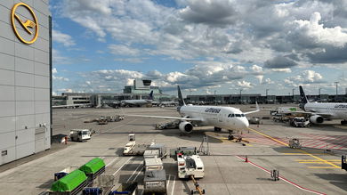 A Lufthansa passenger jet pulls into a terminal gate area on a sunny day.