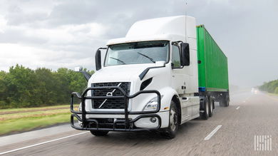 A white sleeper tractor with a green ocean container
