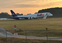 Sunrise over the trees with a damaged FedEx jet sitting in the grass at an airport.