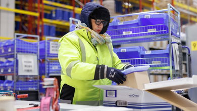 A worker in a yellow parka checks packages in a refrigerated warehouse.
