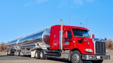 A red KAG Canada tractor pulling two liquid tank trailers