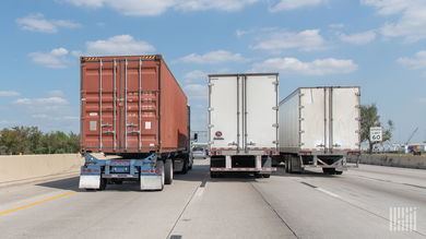 A rear view of one ocean container and two dry van trailers being pulled on a highway