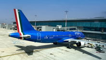 A bright blue ITA Airways plane parked at an airport gate.