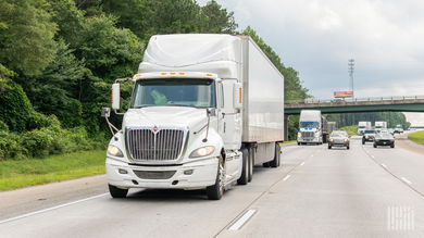 A white tractor pulling a trailer on a highway
