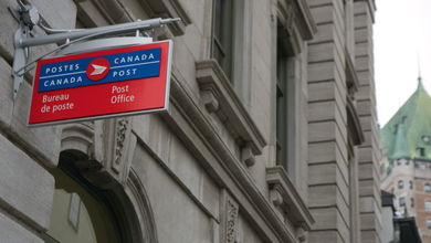 A view of a Canada Post post office sign hanging from a city building.