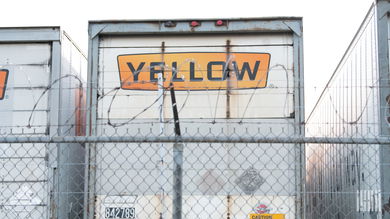 A Yellow trailer parked along a fence at a terminal