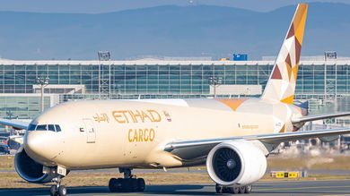 An Etihad Cargo 777 freighter with gold accents on an airport runway.