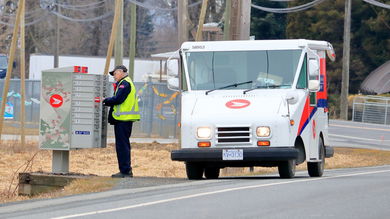 A Canada Post mail carrier makes a stop at a letter box. White van with red lettering.