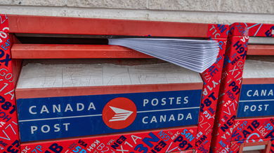 Close up view of envelopes in the mail slot of a red/blue Canada Post drop box.