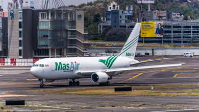 A MasAir cargo jet moves into position at the end of a runway with city buildings visible in the background.